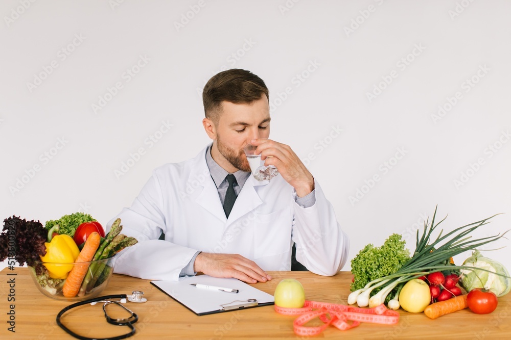 Happy doctor nutritionist sitting at workplace at desk in office among fresh vegetables and drinking water, diet plan concept Happy doctor nutritionist sitting at workplace at desk in office among fresh vegetables and drinking water, diet plan concept