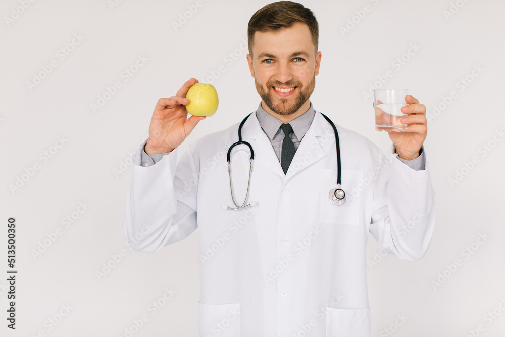The happy male nutritionist doctor with stethoscope smiling and holding water and apple on white background, diet plan concept The happy male nutritionist doctor with stethoscope smiling and holding water and apple on white background, diet plan concept