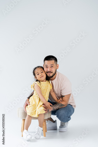 full length of happy asian girl in summer dress standing near father on grey.