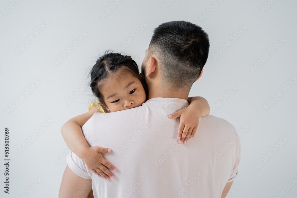 back view of father with beard holding in arms asian preschooler daughter isolated on grey. back view of father with beard holding in arms asian preschooler daughter isolated on grey.