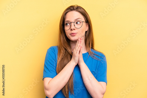Young caucasian woman isolated on yellow background praying, showing devotion, religious person looking for divine inspiration.