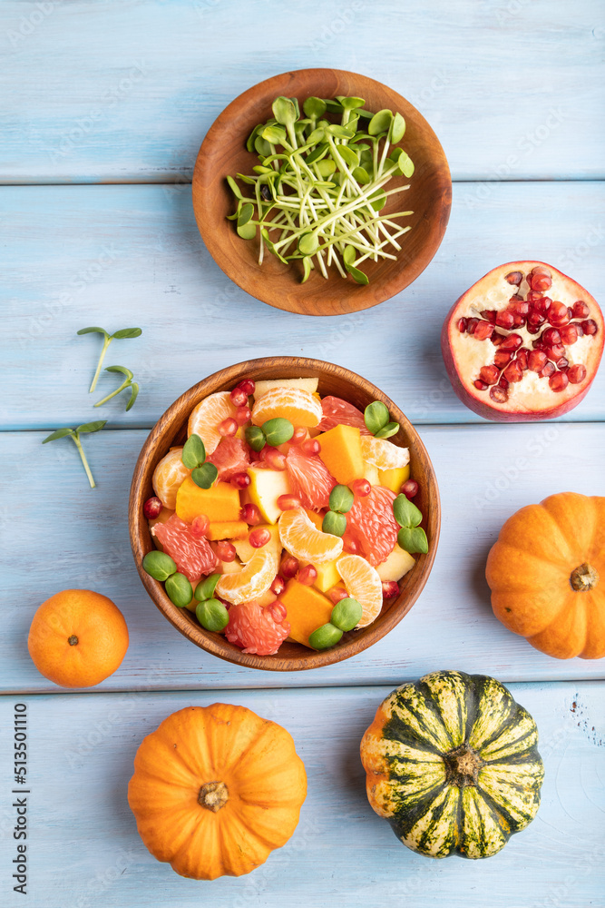 Vegetarian fruit salad of pumpkin, tangerine, pomegranate, microgreen sprouts on blue, top view, close up.