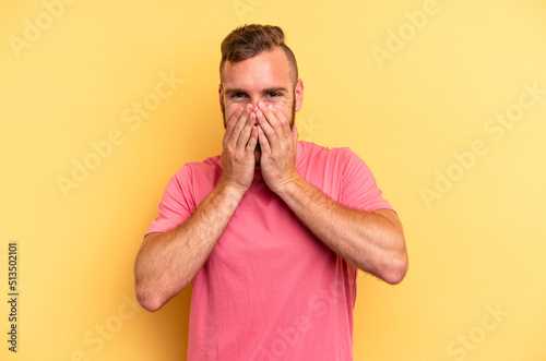 Young caucasian man isolated on yellow background laughing about something, covering mouth with hands.