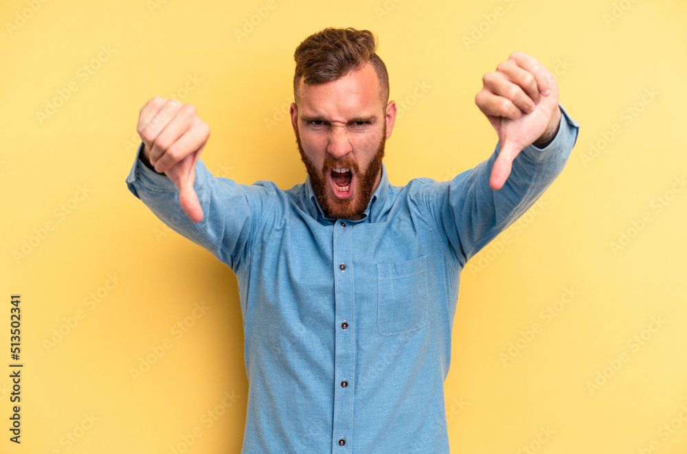 Young caucasian man isolated on yellow background showing thumb down and expressing dislike. Young caucasian man isolated on yellow background showing thumb down and expressing dislike.