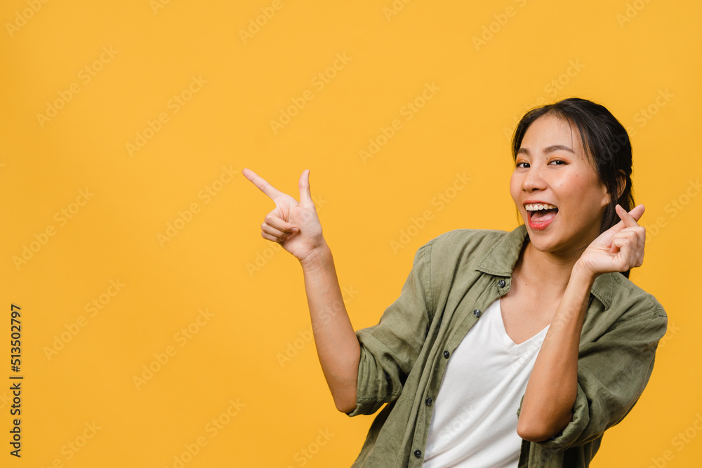 Portrait of young Asian lady smiling with cheerful expression, shows something amazing at blank space in casual cloth and looking at camera isolated over yellow background. Facial expression concept. Portrait of young Asian lady smiling with cheerful expression, shows something amazing at blank space in casual cloth and looking at camera isolated over yellow background. Facial expression concept.