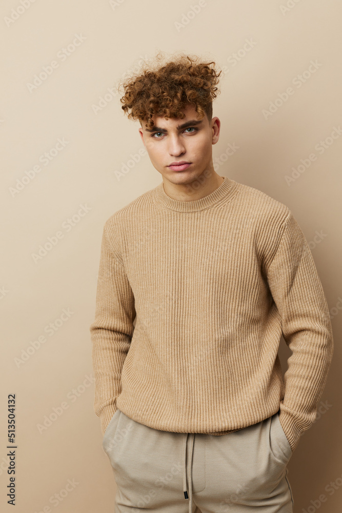 a handsome, attractive man with curly hair, in stylish clothes stands on a beige background and poses relaxed a handsome, attractive man with curly hair, in stylish clothes stands on a beige background and poses relaxed