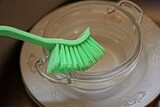 dirty wet white plate and glass cup cleans with a green plastic brush in the kitchen