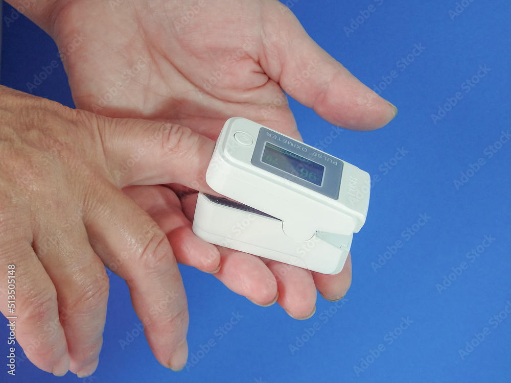 Woman using fingertip pulse oximeter on blue background, top view