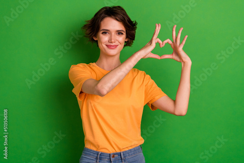 Photo of pretty dreamy young woman dressed orange t-shirt showing arms heart smiling isolated green color background