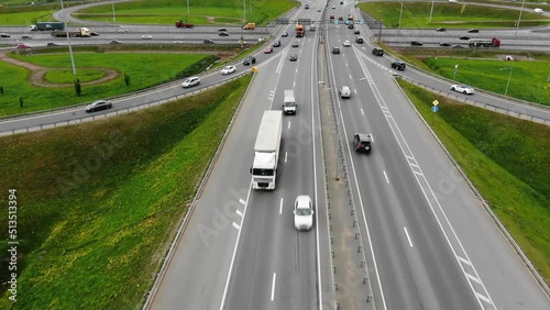 Cars drive on wide highways with multi-level intersection and two-way traffic interchange. Large motorway among green fields connecting big cities aerial view photo