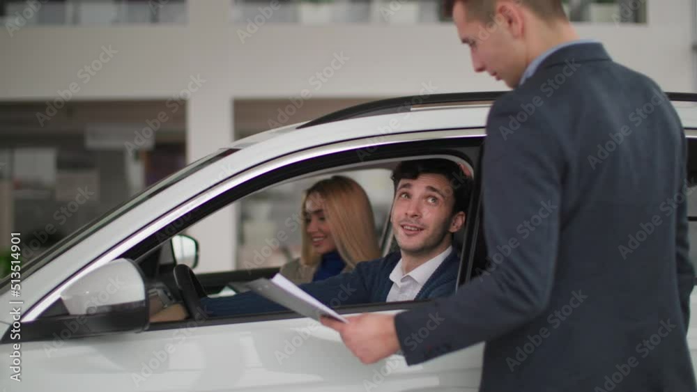 buying car, happy man with family sitting behind wheel of a new auto and talking to dealer in automobile dealership buying car, happy man with family sitting behind wheel of a new auto and talking to dealer in automobile dealership