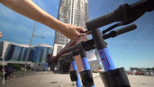 Close-up of women's hands hold phone near modern urban electric scooter, about to unlock it. Modern urban transport. uses eco transport in city center. slow motion