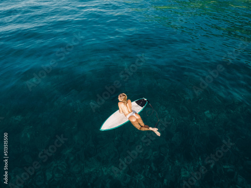 Surf girl relax on surfboard in transparent ocean. Aerial view