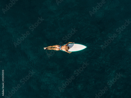 Pretty surfer woman floating on surfboard in ocean. Aerial view
