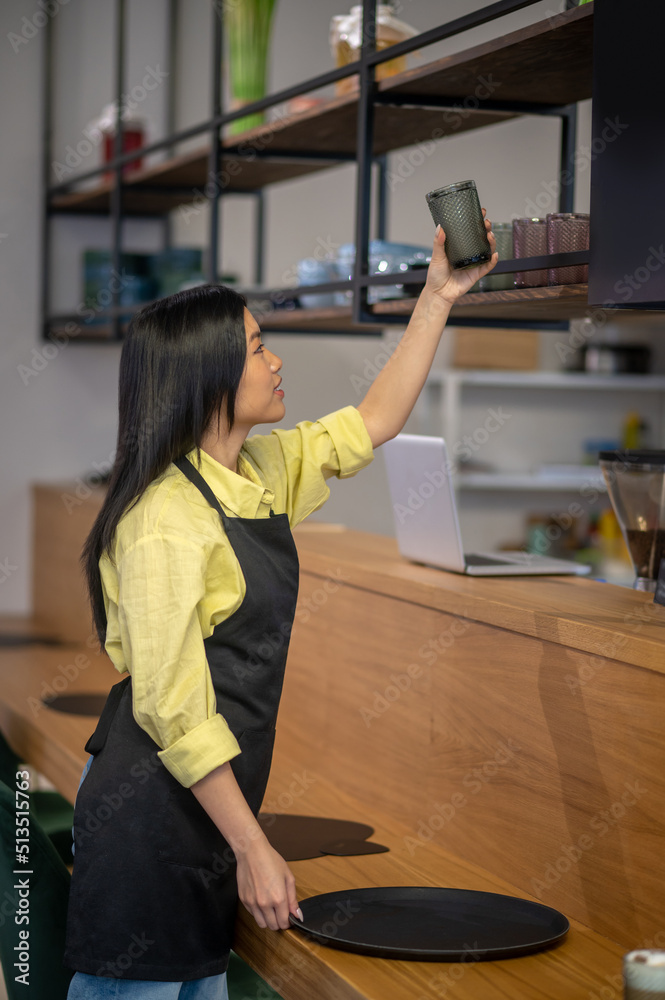 Woman sideways to camera placing glass on top shelf Woman sideways to camera placing glass on top shelf