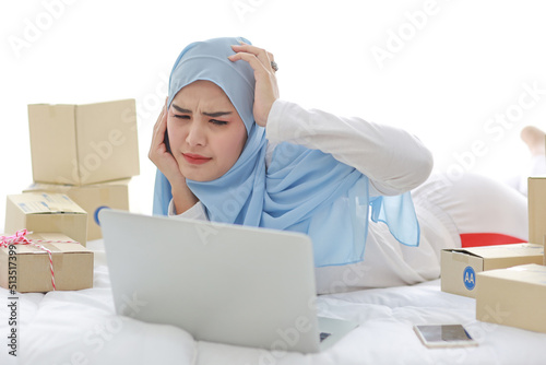 Beautiful and young asian woman in muslim sleepwear with headache emotion lies on bed with computer, mobile phone and online package box delivery. Smart girl with hijab receive bad news and tired © feeling lucky