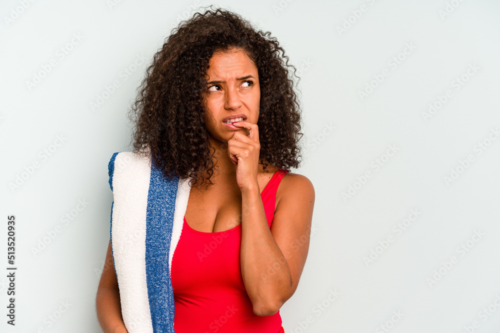 Young brazilian woman going to the beach holding a towel isolated on blue background relaxed thinking about something looking at a copy space. Young brazilian woman going to the beach holding a towel isolated on blue background relaxed thinking about something looking at a copy space.