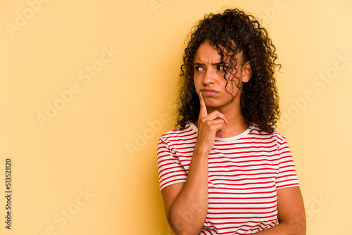 Young Brazilian woman isolated on yellow background looking sideways with doubtful and skeptical expression. photo
