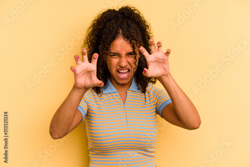Young Brazilian woman isolated on yellow background showing claws imitating a cat  aggressive gesture.