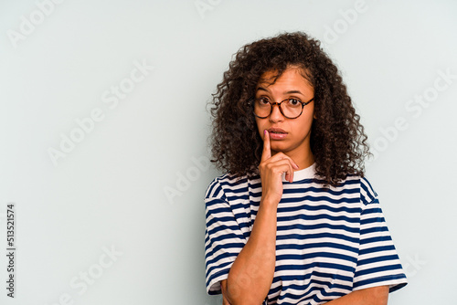 Young Brazilian woman isolated on blue background looking sideways with doubtful and skeptical expression. © Asier