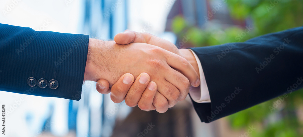 Confident businessman and his colleague are shaking hands in front of modern office building. Financial investors outdoor. Banking and business.