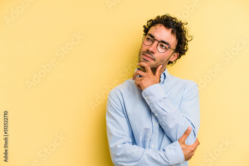Young caucasian man isolated on yellow background relaxed thinking about something looking at a copy space. © Asier