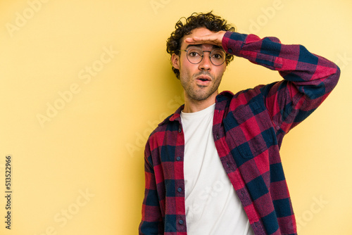 Young caucasian man isolated on yellow background looking far away keeping hand on forehead.