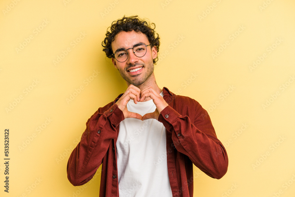 Young caucasian man isolated on yellow background smiling and showing a heart shape with hands.