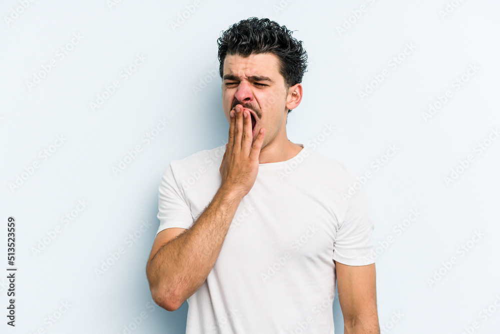 Young caucasian man isolated on blue background yawning showing a tired gesture covering mouth with hand. Young caucasian man isolated on blue background yawning showing a tired gesture covering mouth with hand.