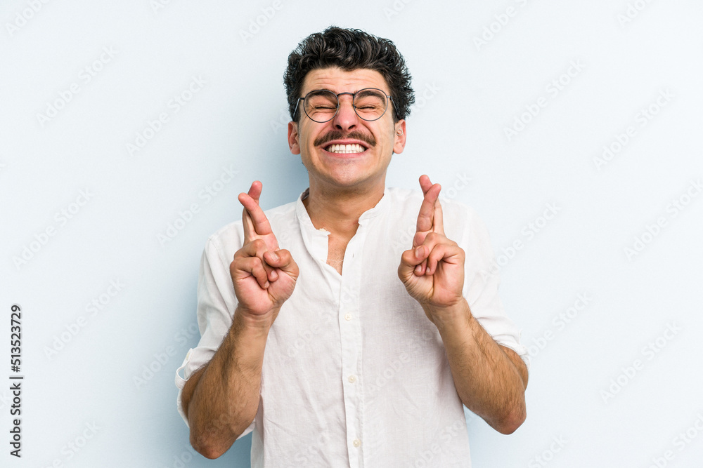 Young caucasian man isolated on blue background crossing fingers for having luck Young caucasian man isolated on blue background crossing fingers for having luck