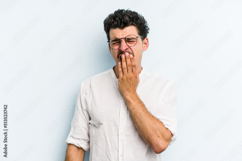 Young caucasian man isolated on blue background yawning showing a tired gesture covering mouth with hand. Young caucasian man isolated on blue background yawning showing a tired gesture covering mouth with hand.