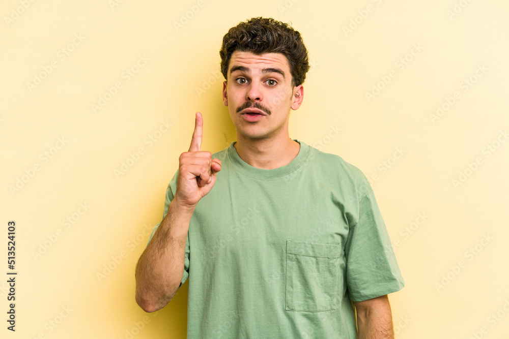 Young caucasian man isolated on yellow background pointing upside with opened mouth. Young caucasian man isolated on yellow background pointing upside with opened mouth.
