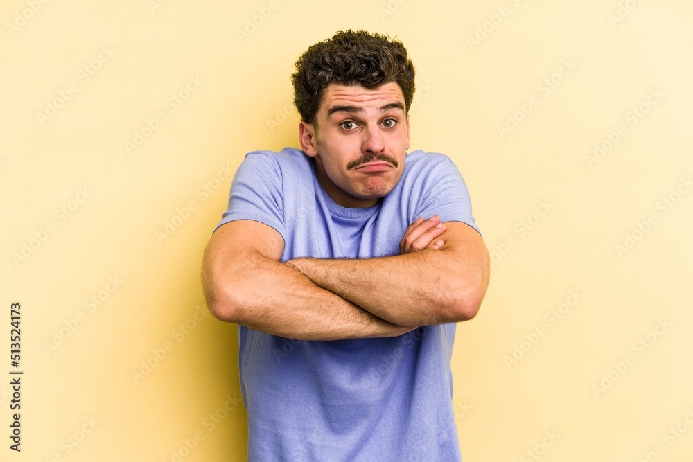 Young caucasian man isolated on yellow background shrugs shoulders and open eyes confused. Young caucasian man isolated on yellow background shrugs shoulders and open eyes confused.
