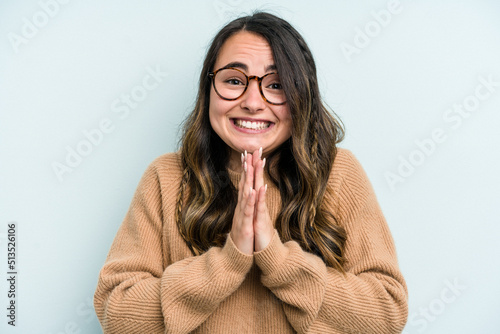 Young caucasian woman isolated on blue background holding hands in pray near mouth, feels confident. photo