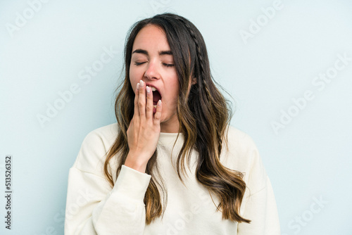 Young caucasian woman isolated on blue background yawning showing a tired gesture covering mouth with hand.