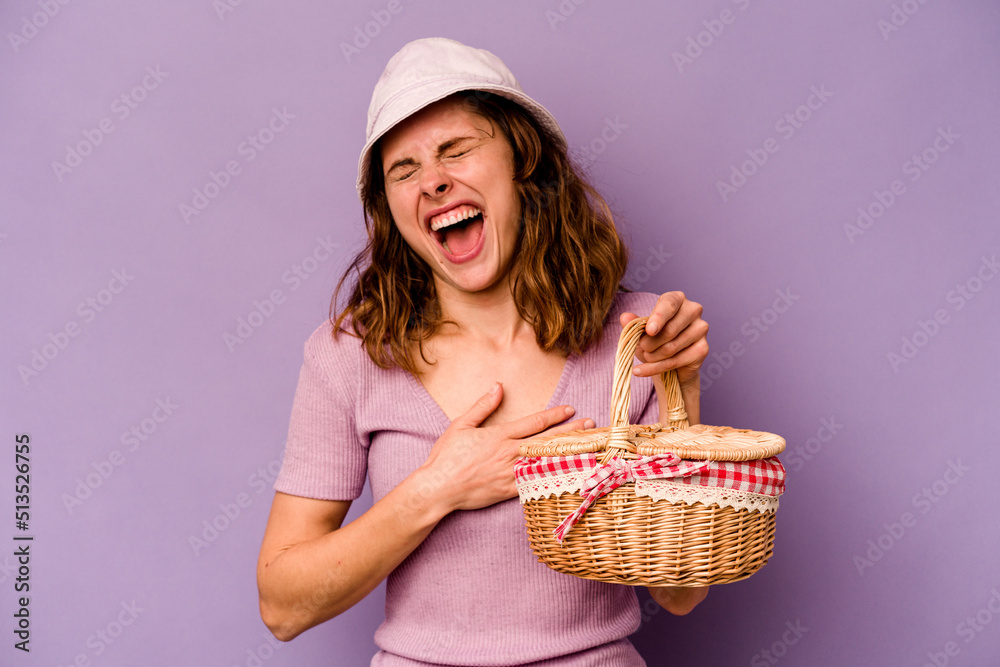 Young caucasian woman going on a picnic isolated on purple background laughs out loudly keeping hand on chest. Young caucasian woman going on a picnic isolated on purple background laughs out loudly keeping hand on chest.