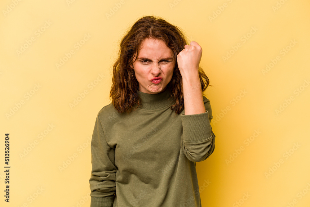 Young caucasian woman isolated on yellow background showing fist to camera, aggressive facial expression. Young caucasian woman isolated on yellow background showing fist to camera, aggressive facial expression.