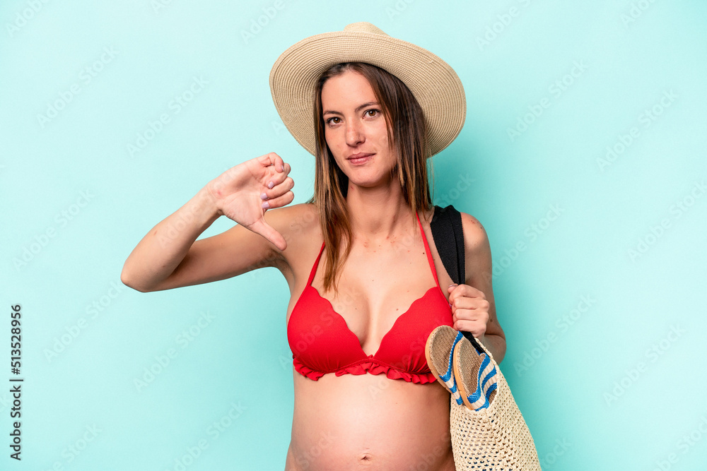 Young caucasian pregnant woman going to the beach isolated on blue background showing a dislike gesture, thumbs down. Disagreement concept. Young caucasian pregnant woman going to the beach isolated on blue background showing a dislike gesture, thumbs down. Disagreement concept.