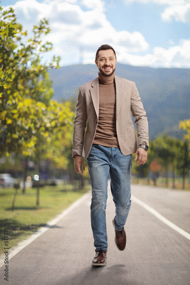 Young man in a beige suit and jeans walking towards camera on an asphalt pedestrian lane Young man in a beige suit and jeans walking towards camera on an asphalt pedestrian lane