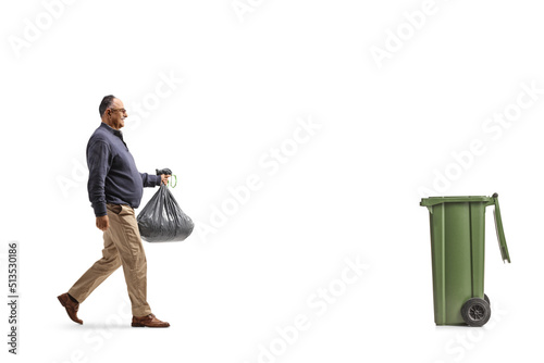 Full length profile shot of a mature man carrying a plastic waste bag and walking towards a dustbin photo