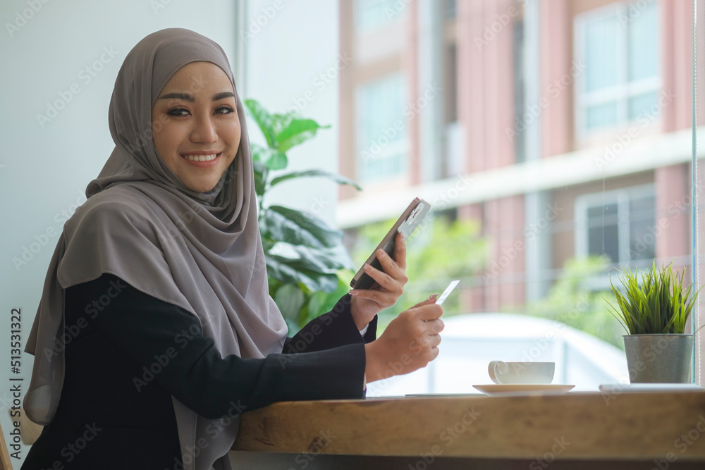 Smiling Islamic woman in hijab holding credit card and smart phone for internet banking or online shopping. Smiling Islamic woman in hijab holding credit card and smart phone for internet banking or online shopping.