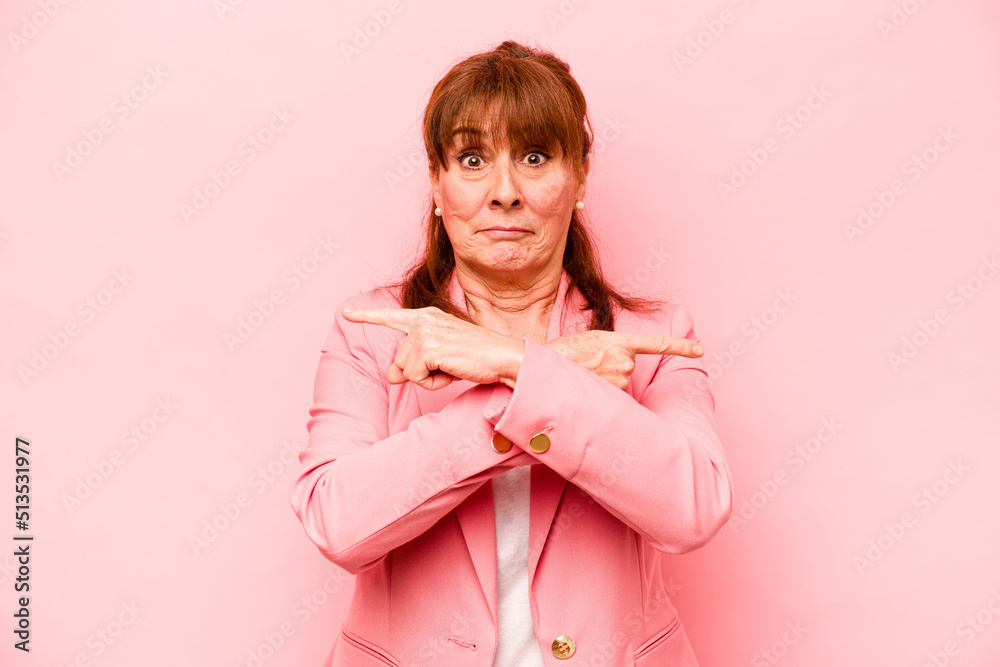 Middle age caucasian woman isolated on pink background points sideways, is trying to choose between two options. Middle age caucasian woman isolated on pink background points sideways, is trying to choose between two options.