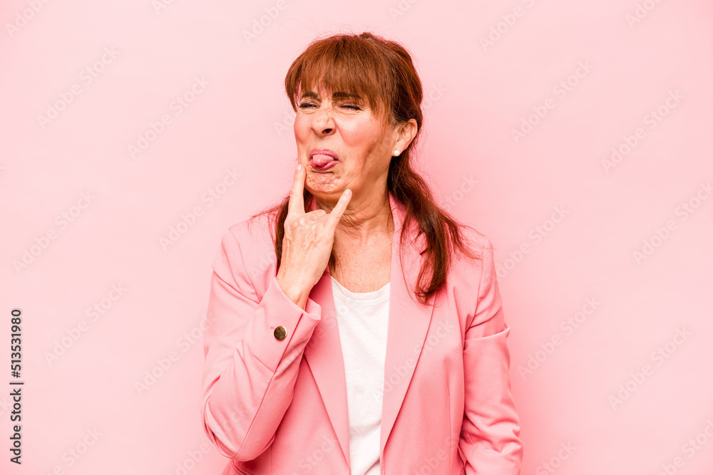 Middle age caucasian woman isolated on pink background showing rock gesture with fingers Middle age caucasian woman isolated on pink background showing rock gesture with fingers