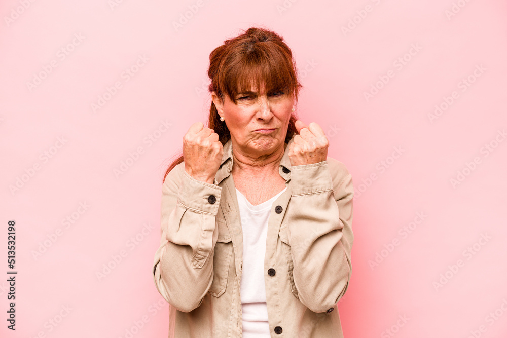 Middle age caucasian woman isolated on pink background showing fist to camera, aggressive facial expression. Middle age caucasian woman isolated on pink background showing fist to camera, aggressive facial expression.