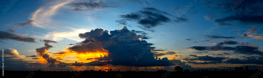 Panorama photo of Landscape sunset with dark clouds.Tree silhouetted against a setting sun.Dark tree on open field dramatic sunrise and blue sky. Panorama photo of Landscape sunset with dark clouds.Tree silhouetted against a setting sun.Dark tree on open field dramatic sunrise and blue sky.