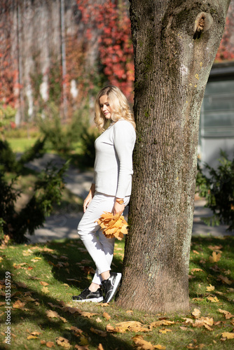 Vertical portrait of beautiful woman against background of blurry autumn park and holding bouquet of leaves.