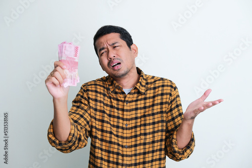 Adult Asian man showing sad expression when looking to paper money that he hold photo