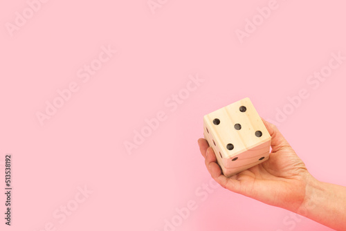 Cuadro en lienzo Mano de mujer sosteniendo un dado de madera sobre un fondo rosa liso y aislado