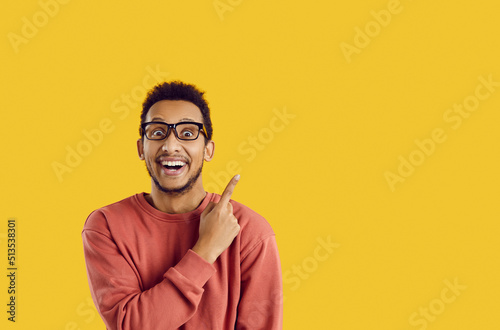 Happy excited cheerful ethnic black college or university student smiling and doing pointing gesture at cool solution, good idea, useful contact phone number on text copyspace background on right side photo