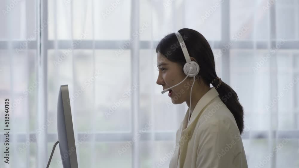 Call center Asian woman, call center employee of an internet customer service company, help customers by phone. In a formal suit wearing a headset or headphones talks to customers in a modern office. Call center Asian woman, call center employee of an internet customer service company, help customers by phone. In a formal suit wearing a headset or headphones talks to customers in a modern office.